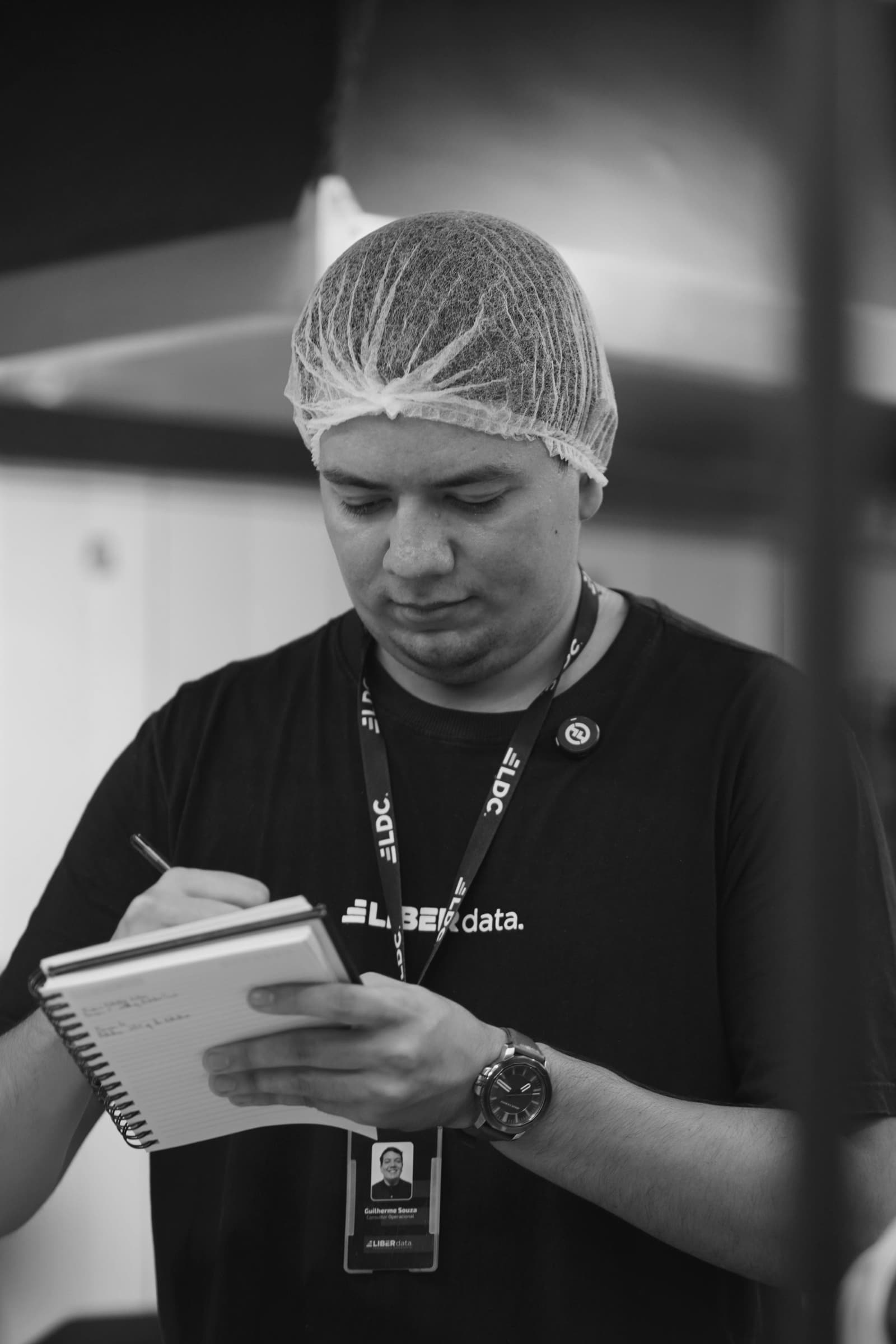 Consultor da Liberdata anotando em bloco dentro da cozinha de um cliente, de touca e camiseta da empresa.