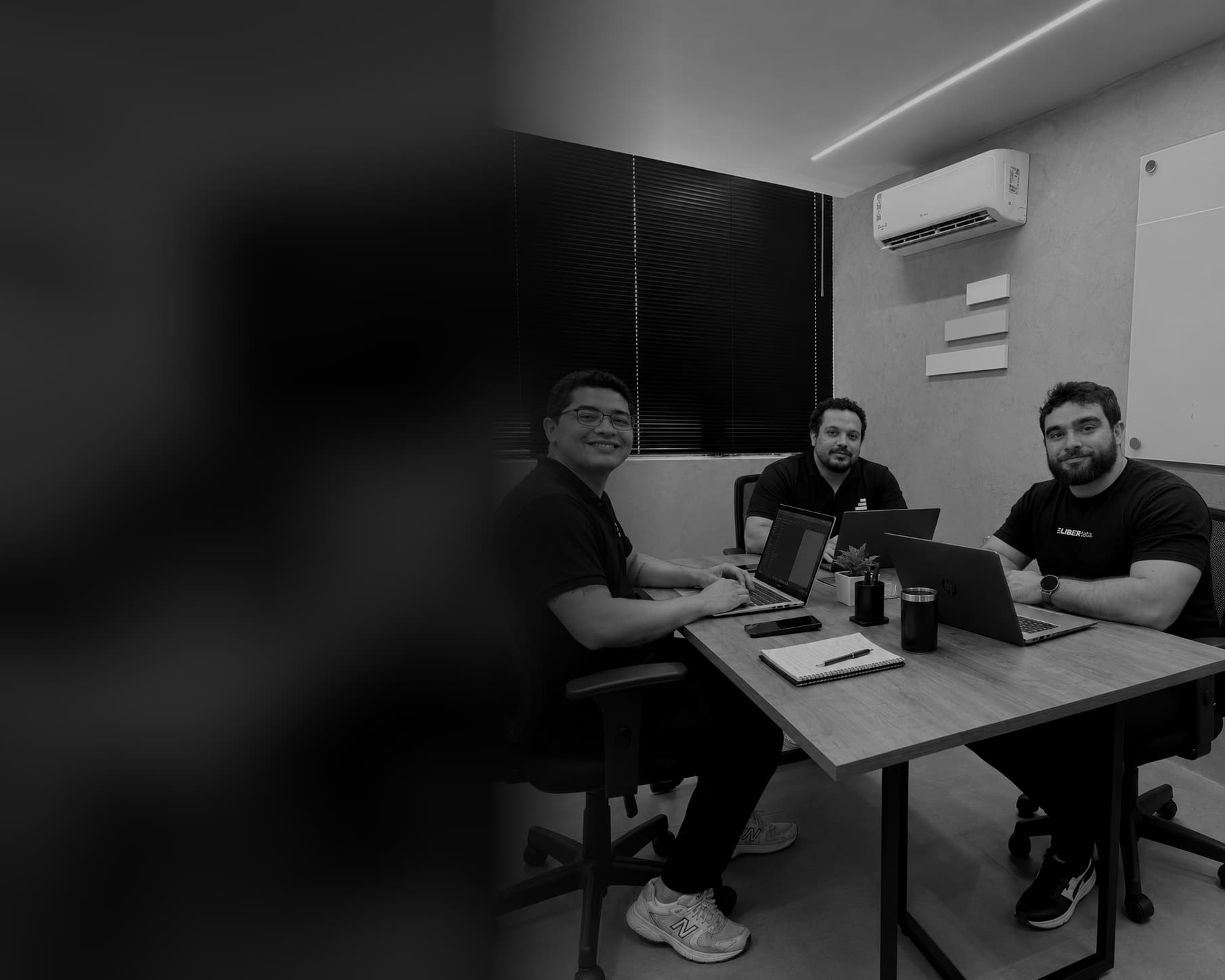 Os três sócios da Liberdata sentados em volta de uma mesa de reunião na sede, com notebooks abertos.